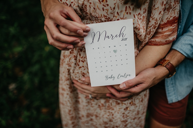 Couple holds a mini calendar marking their due date for their pregnancy announcement