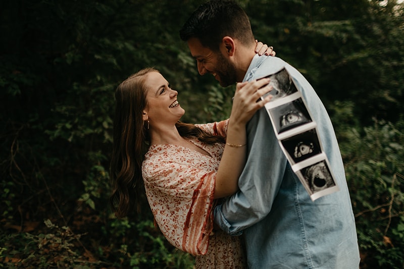 Couple stands arm in arm holding sonogram of their pregnancy